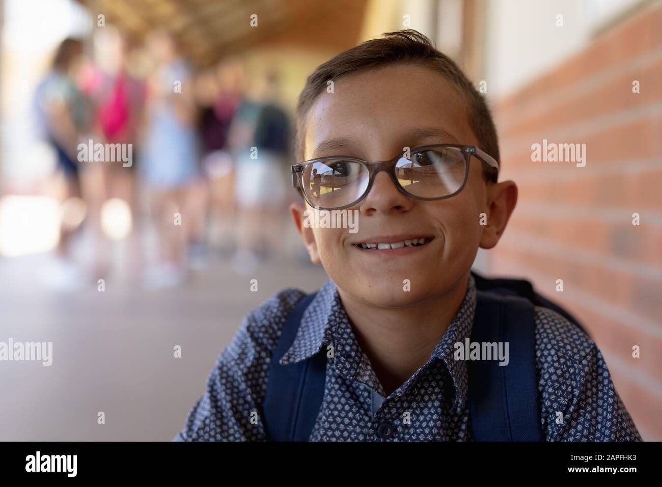 scolaretto che indossa gli occhiali seduti da un muro nel cortile della scuola elementare Foto Stock