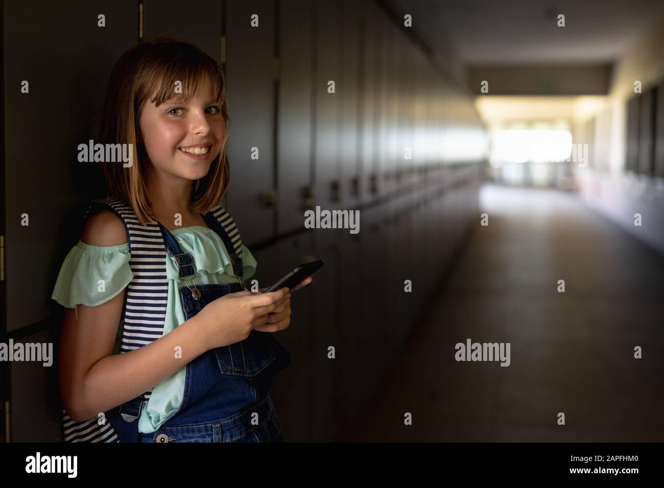 schoolgirl appoggiato contro gli armadietti in un corridoio utilizzando uno smartphone Foto Stock