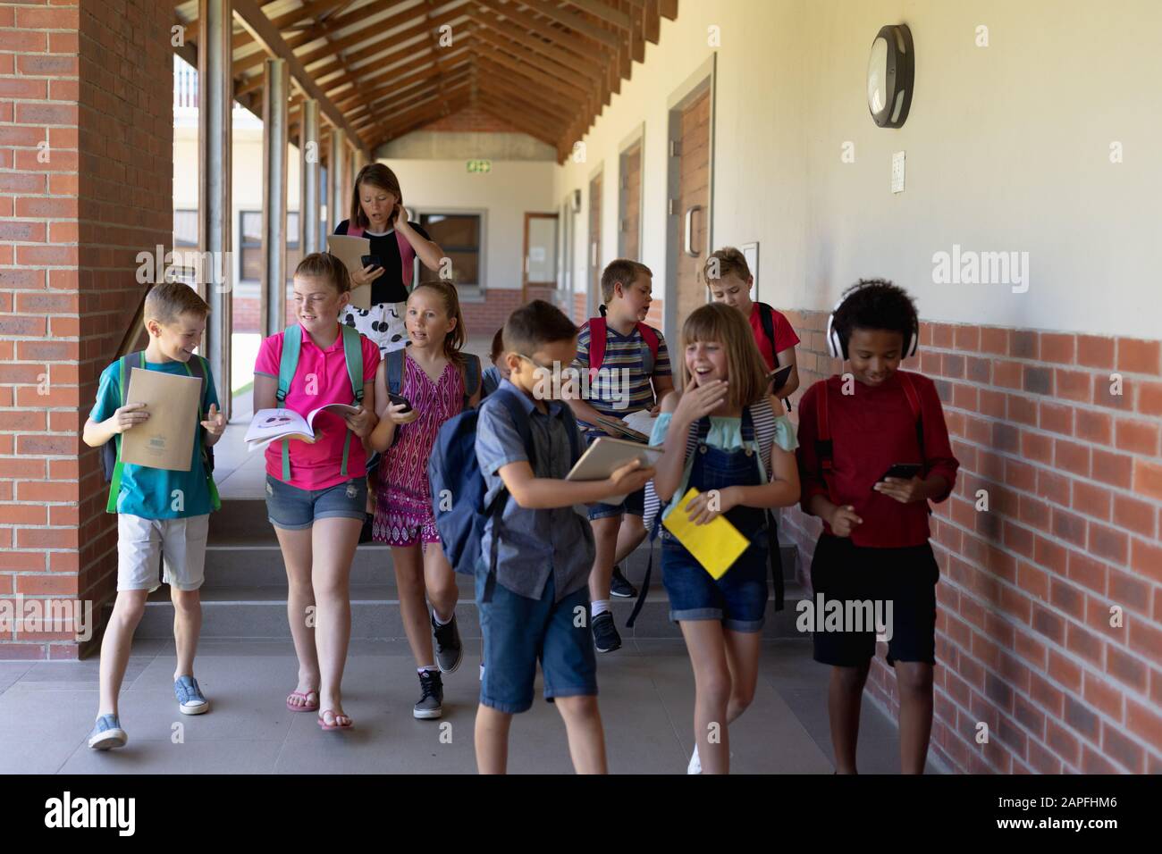Gruppo di alunni che camminano in un corridoio esterno della scuola elementare Foto Stock