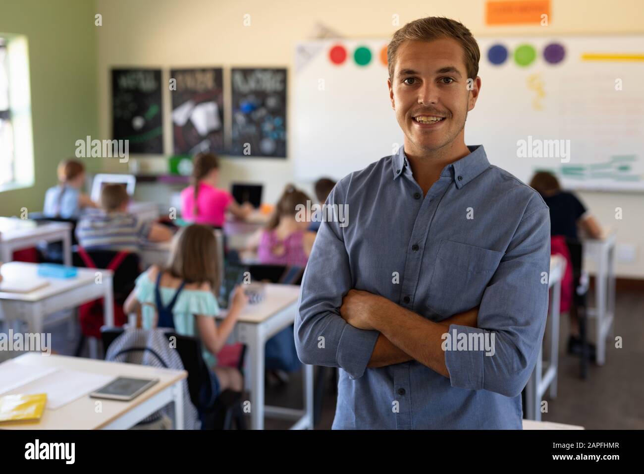 Insegnante di scuola maschile in piedi con le braccia incrociate in una scuola elementare classe Foto Stock