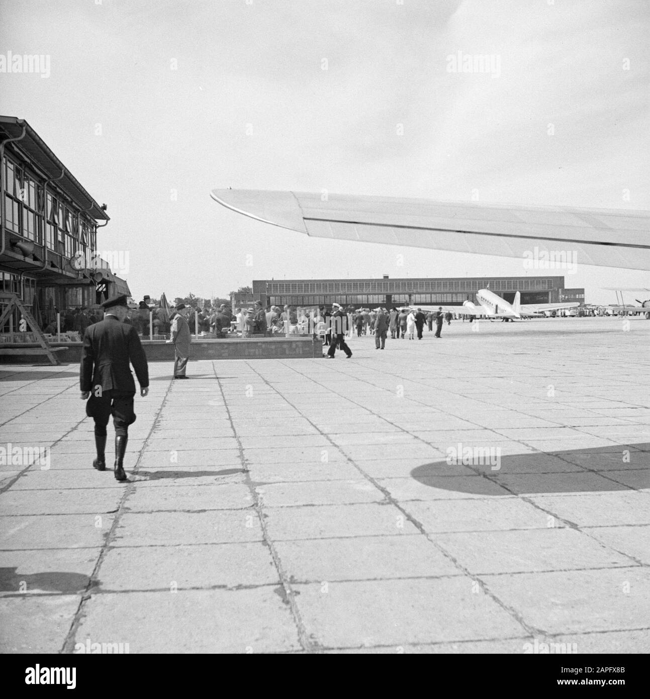 Aeroporto Schiphol Descrizione: Café-Terrace la vista ampia con sullo sfondo un grande hangar e un Douglas DC-3 parcheggiato all'aeroporto di Schiphol Data: 1936 posizione: Amsterdam, Noord-Holland Parole Chiave: Esterno, edifici, compagnie aeree, viaggiatori, aerei, aeroporti Nome istituto: Schiphol Foto Stock