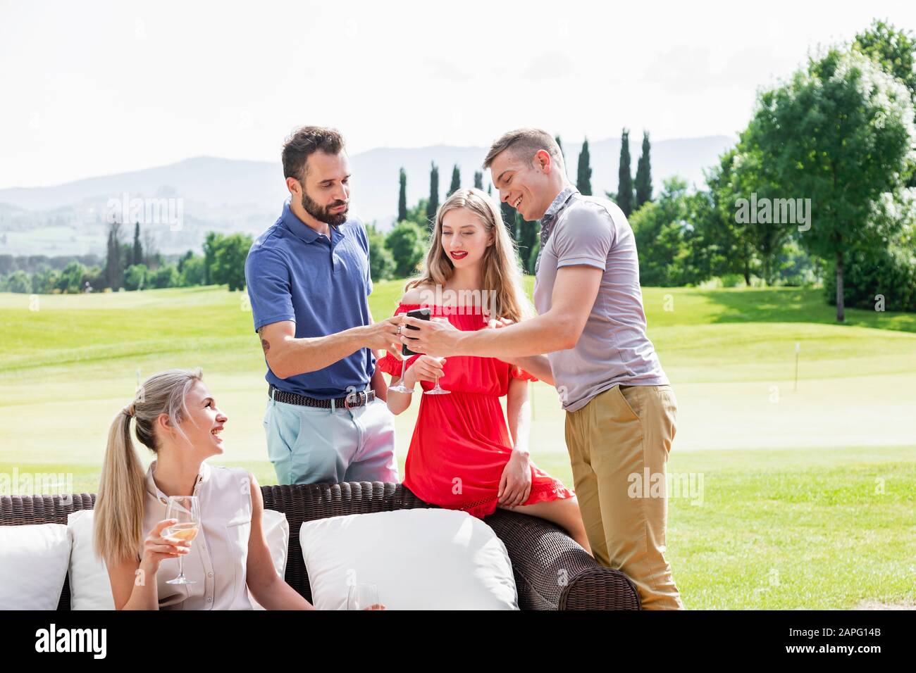 Gli amici si godono il vino e parlano sul divano sul campo da golf Foto Stock
