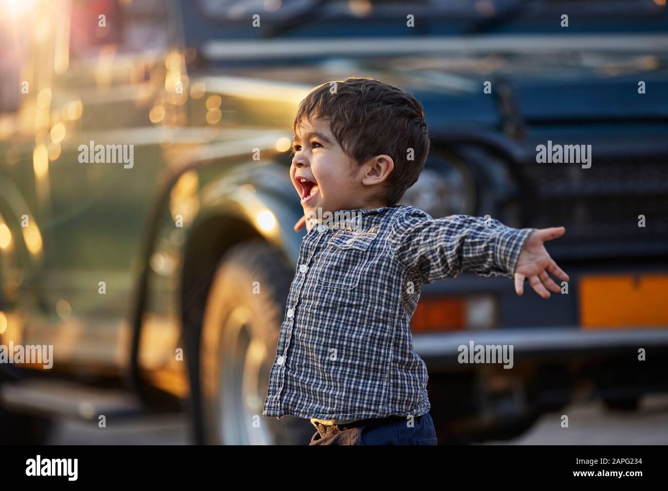Bambino eccitato con braccia aperte in piedi da un grande veicolo Foto Stock
