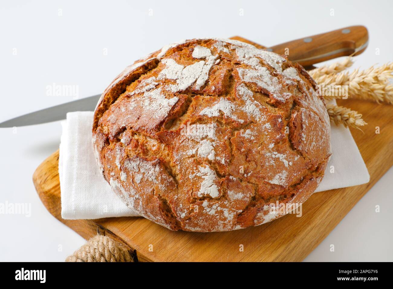 Pagnotta di pane rustico, spighe di grano e coltello da cucina sul tagliere Foto Stock