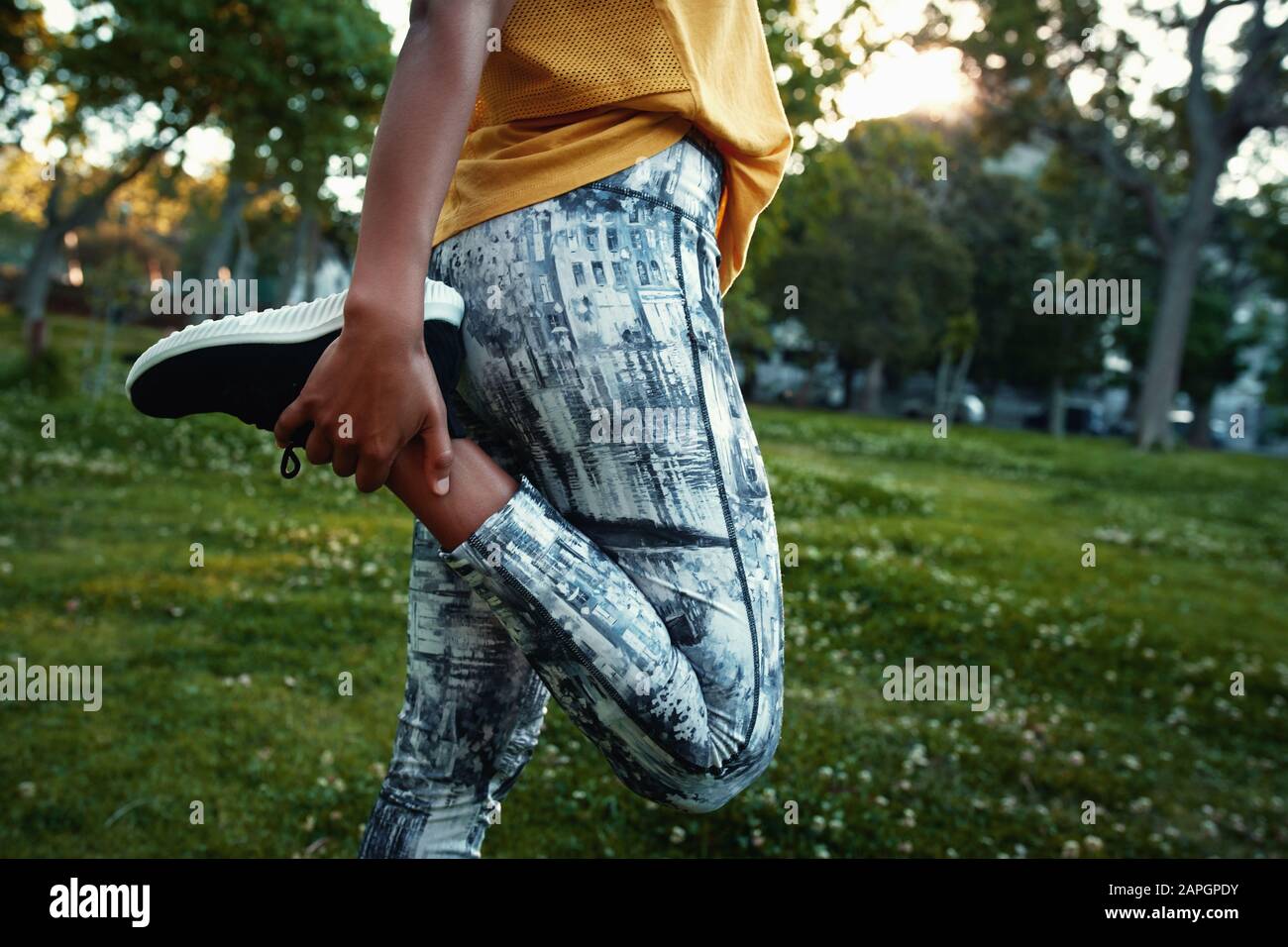 Primo piano di donna in abbigliamento sportivo che allunga la gamba nel parco - donna che allunga le sue quads prima di una corsa Foto Stock