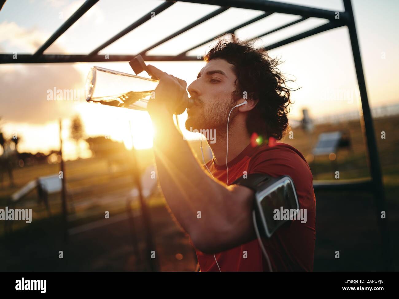 Giovane assetato che ha una pausa bere una bottiglia riutilizzabile di acqua alla luce del sole nel parco della palestra Foto Stock