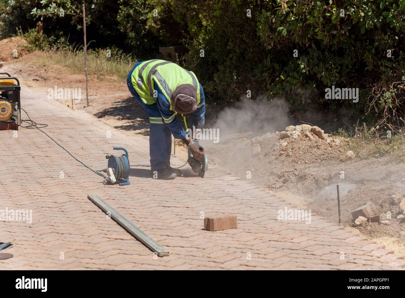 Rooiels, Capo Occidentale, Sud Africa. Dicembre 2019. Lavoratore che utilizza una smerigliatrice elettrica per finire la posa di una strada pavimentata in mattoni. Foto Stock