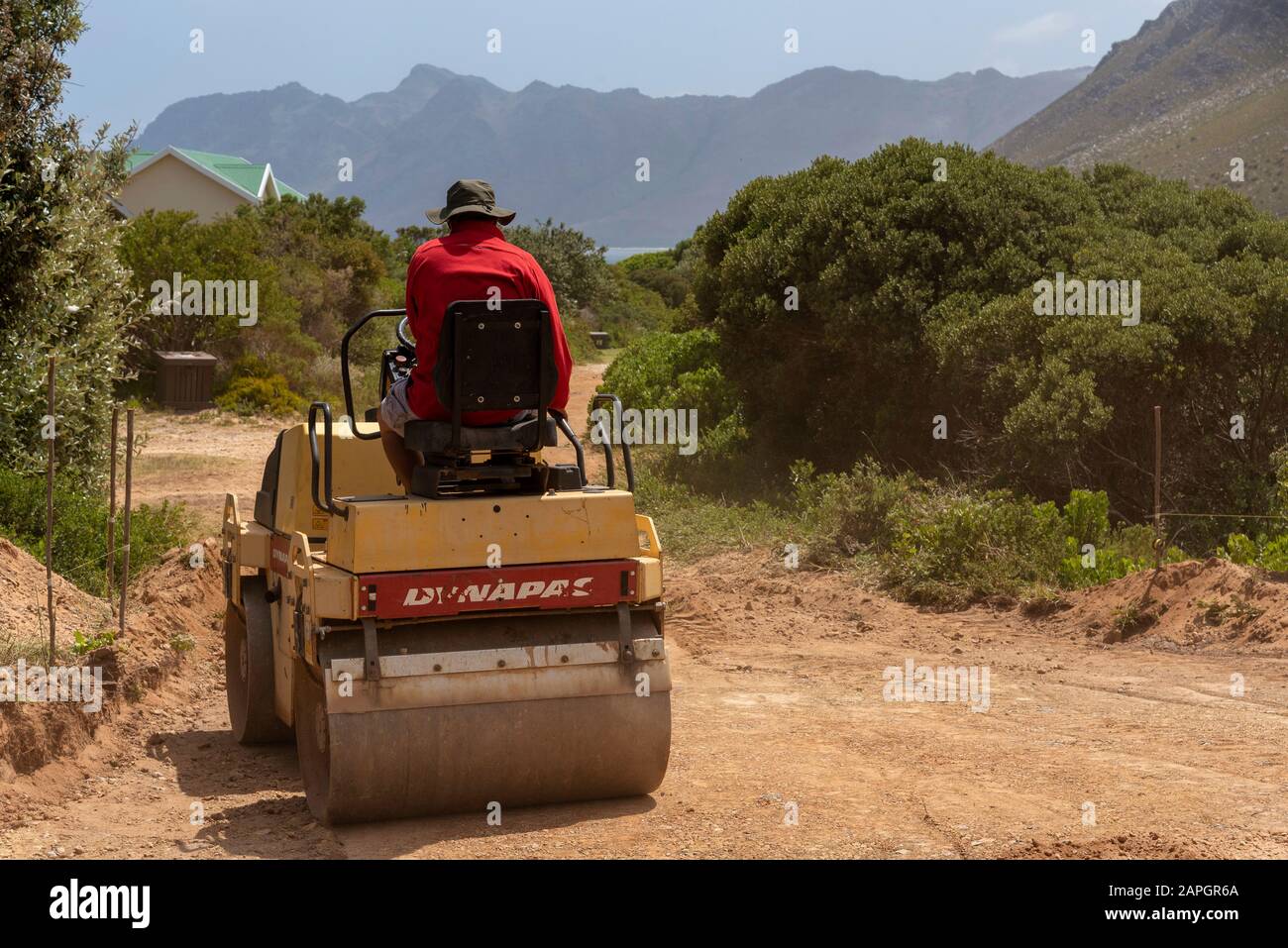 Rooiels, Capo Occidentale, Sud Africa. Dicembre 2019. Lavoratore terra di rotolamento per preparare il terreno per porre una strada in mattoni nel piccolo borgo di Rooiels. Foto Stock