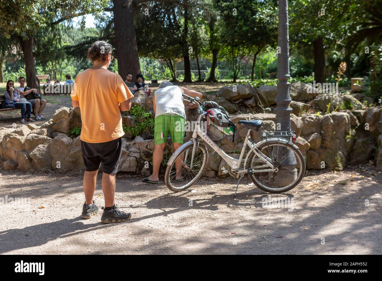L'uomo guarda come un altro uomo beve da una fontana nel parco di Villa Borghese a Roma Foto Stock