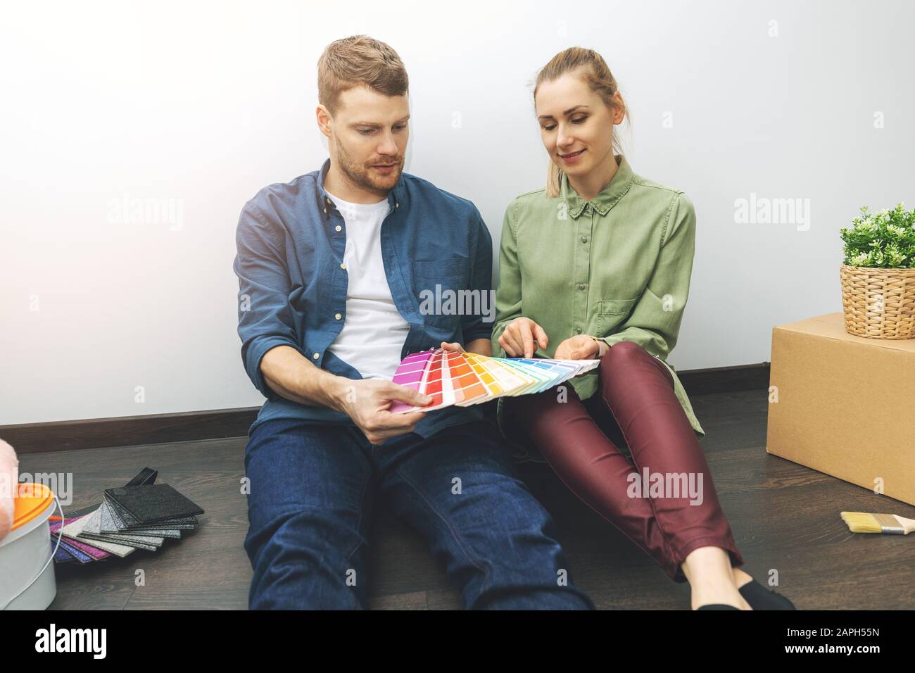 giovane coppia seduto sul pavimento in camera e scegliendo il colore della vernice dai campioni per il nuovo design degli interni Foto Stock