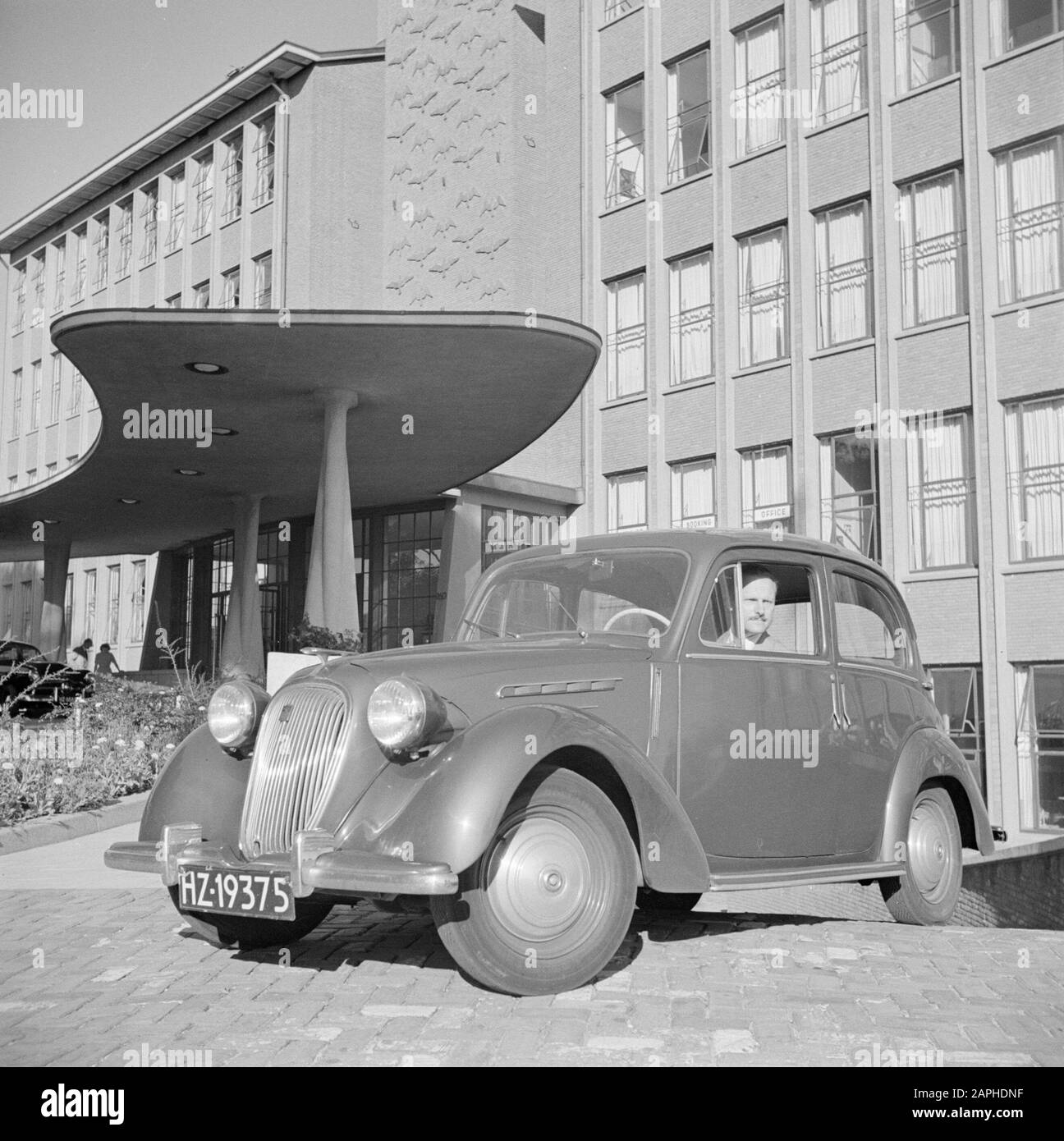Identità aziendale del personale KLM e Schiphol Descrizione: Il Sig. De Visser nella sua Simca 8 di fronte all'edificio principale KLM dell'Aia Data: Agosto 1951 Località: L'Aia, Zuid-Holland Parole Chiave: Automobili, edifici, uomini Nome dell'istituzione: KLM Foto Stock