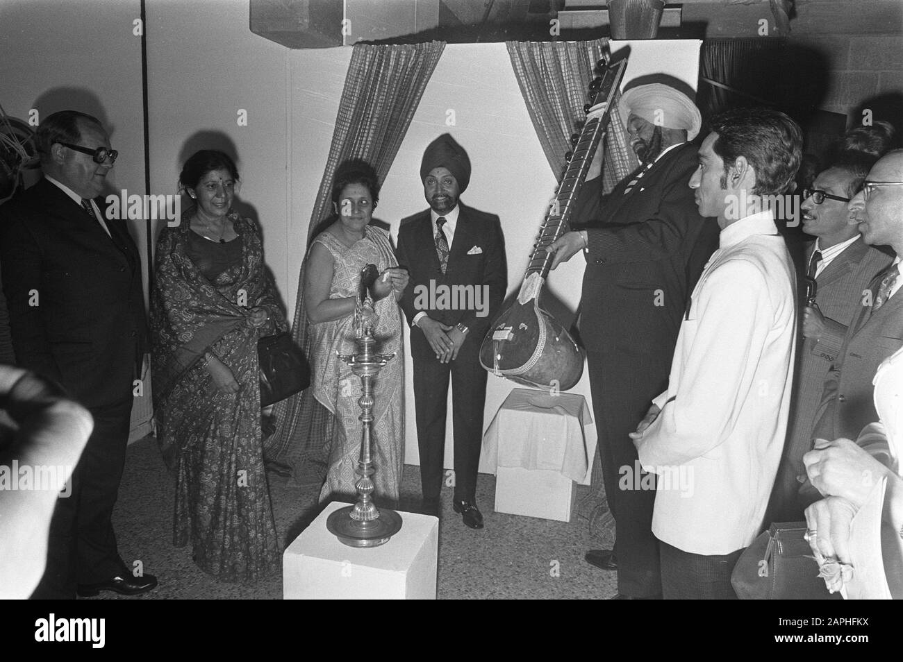Apertura mostra I Musicmakers dell'India a Madurodam Descrizione: Gli espositori indiani della mostra mostrano uno strumento musicale indiano, il sitar - in primo piano una lampada a olio Data: 21 giugno 1972 posizione: Den Haag, Madurodam, Zuid-Holland Parole Chiave: Costumi tradizionali, strumenti musicali, lampade a olio, aperture, mostre Foto Stock