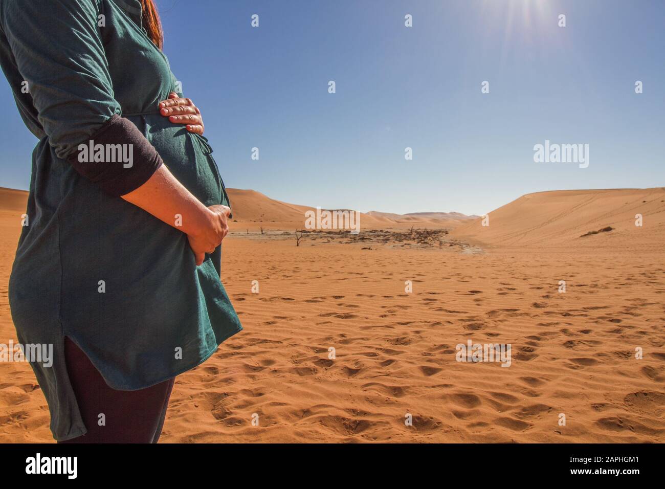 Viaggiare incinta - primo piano di una donna che tiene il suo ventre di fronte alle dune di sabbia di sossusvlei, namibia Foto Stock