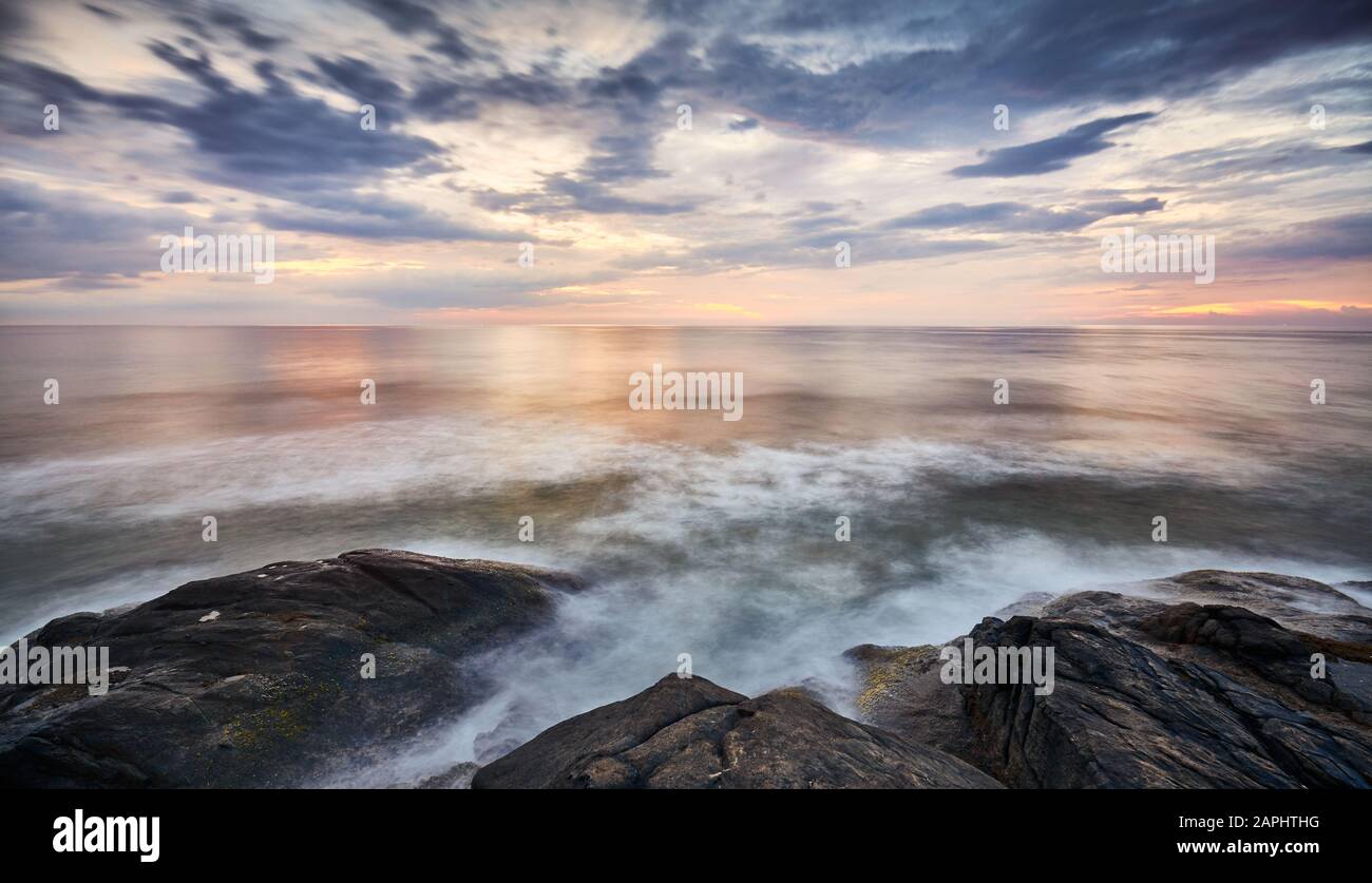 Tramonto panoramico sull'acqua vista dalla costa rocciosa, foto a lunga esposizione. Foto Stock