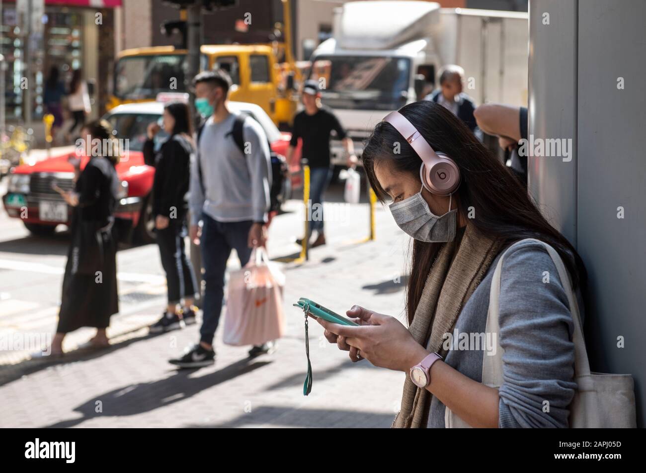 Una donna copre il suo viso con una maschera sanitaria mentre ascolta la musica sulla strada dopo che i primi casi di coronavirus sono stati confermati a Hong Kong. La Cina ha implementato un sistema di trasporto pubblico e un blocco aeroportuale in diverse città per rallentare la diffusione del coronavirus di Wuhan. Foto Stock