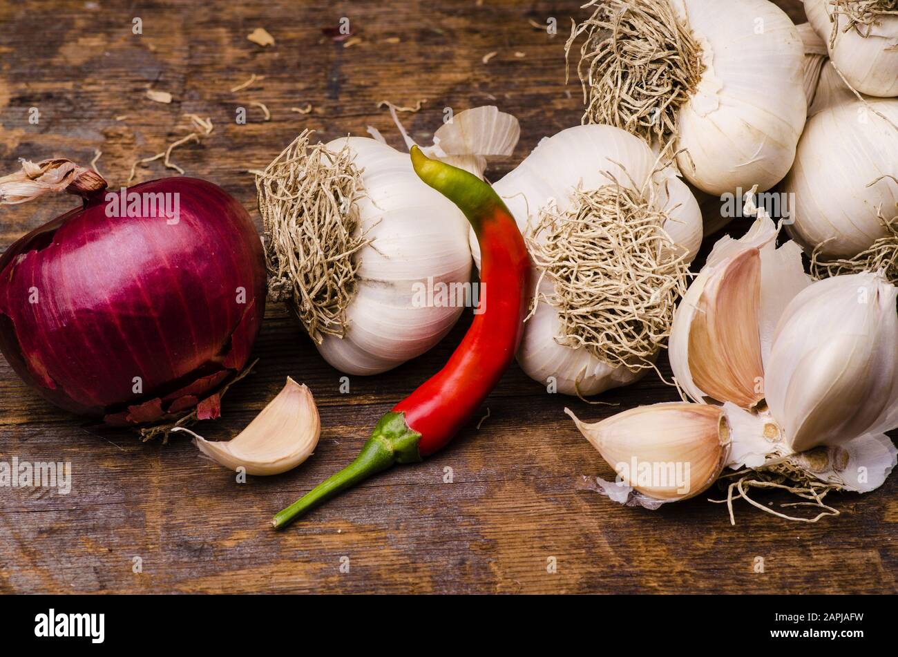 Trecciato aglio secco, una cipolla rossa e peperoncino piccante su rustico tavolo in legno. Ancora vita Foto Stock