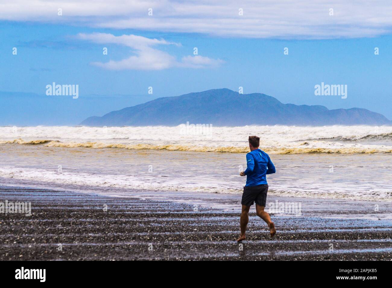 Isola di Kāpiti vista dalla spiaggia di Ōtaki, con un uomo in corsa, Isola del Nord, Nuova Zelanda Foto Stock
