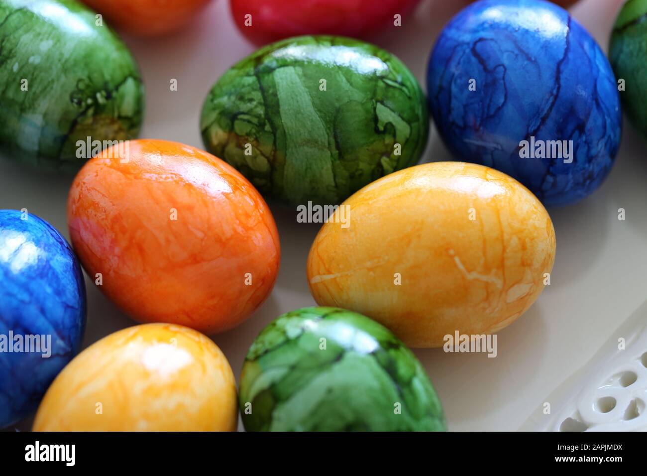 Decorazioni pasquali colorate e gioiose su un tavolo. Immagine a colori di closeup di molteplici uova di Pasqua dipinte con colori felici e vivaci. Foto Stock