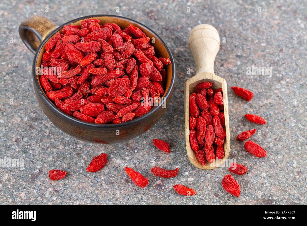 Coppa e cucchiaio di legno con frutti rossi di goji secchi su sfondo grigio di pietra. Vista dall'alto Foto Stock