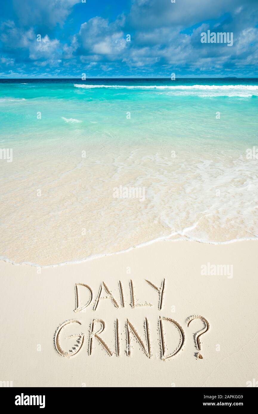 Un divertente messaggio di viaggio invernale 'DAILY GRIND?' scritto a mano sulla sabbia liscia di una spiaggia tropicale dell'isola Foto Stock