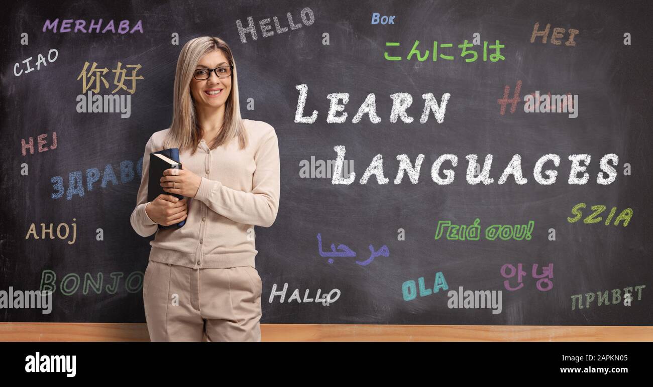 Giovane insegnante di lingua femminile davanti a una lavagna con ciao scritto in diverse lingue Foto Stock