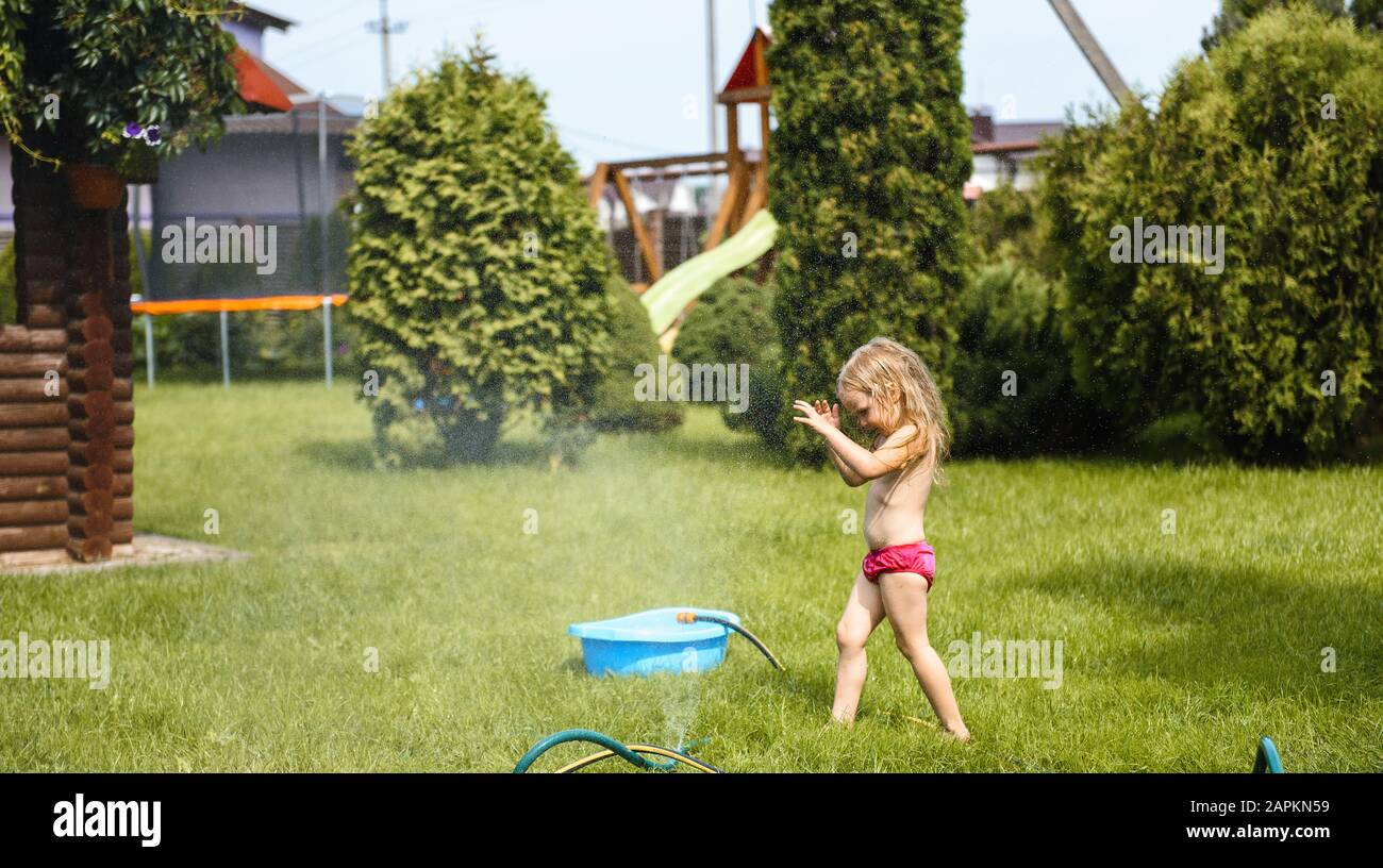 Bambina che gioca con l'acqua nel cortile della casa Foto Stock