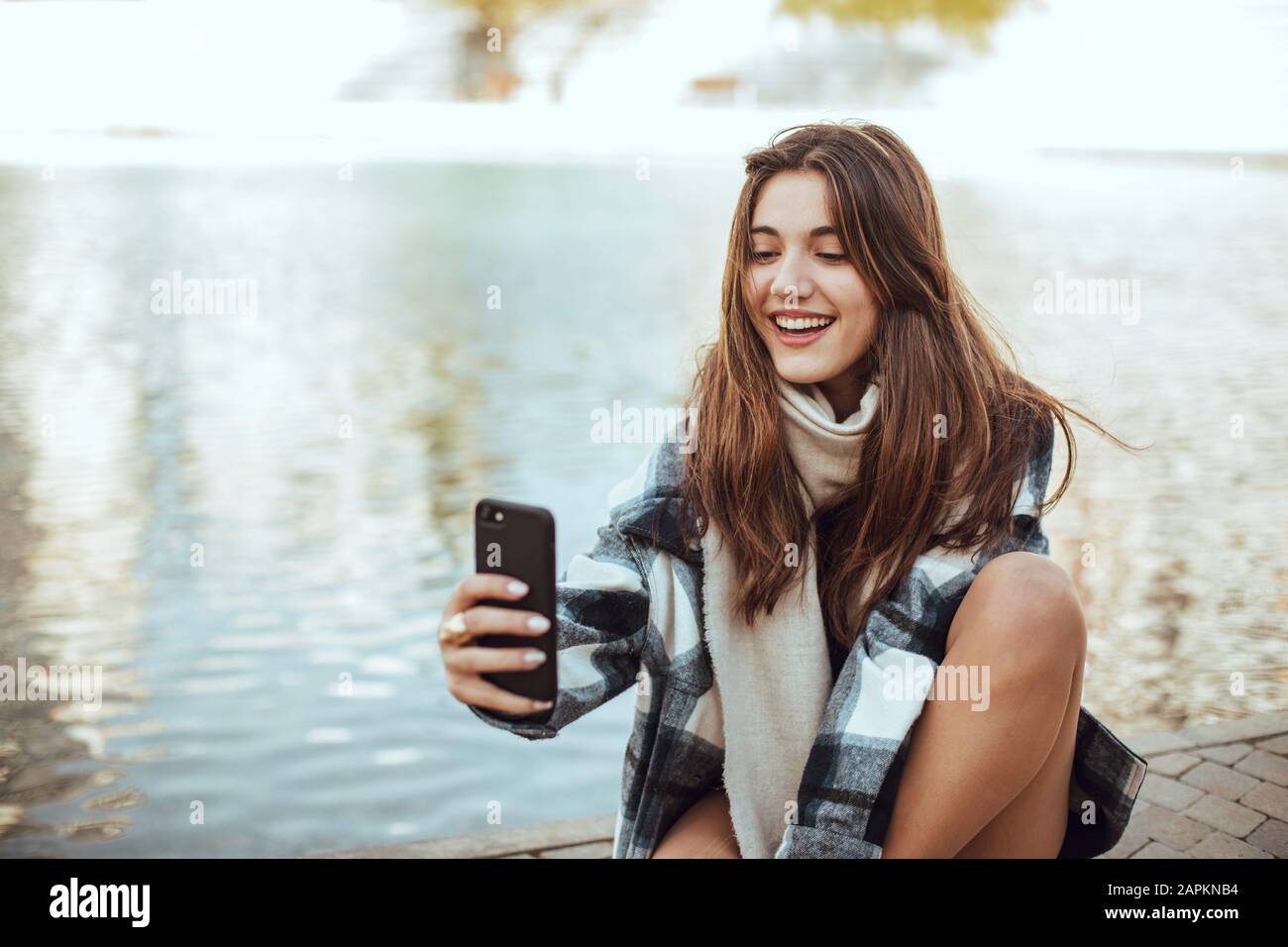 Giovane bruna donna che usa lo smartphone e prende un selfie al lago Foto Stock