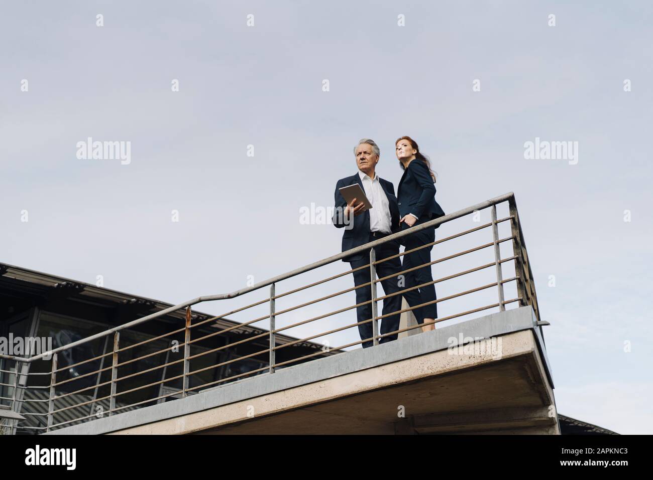 Uomo d'affari e donna d'affari che si trovano su un balcone all'esterno dell'edificio dell'ufficio Foto Stock