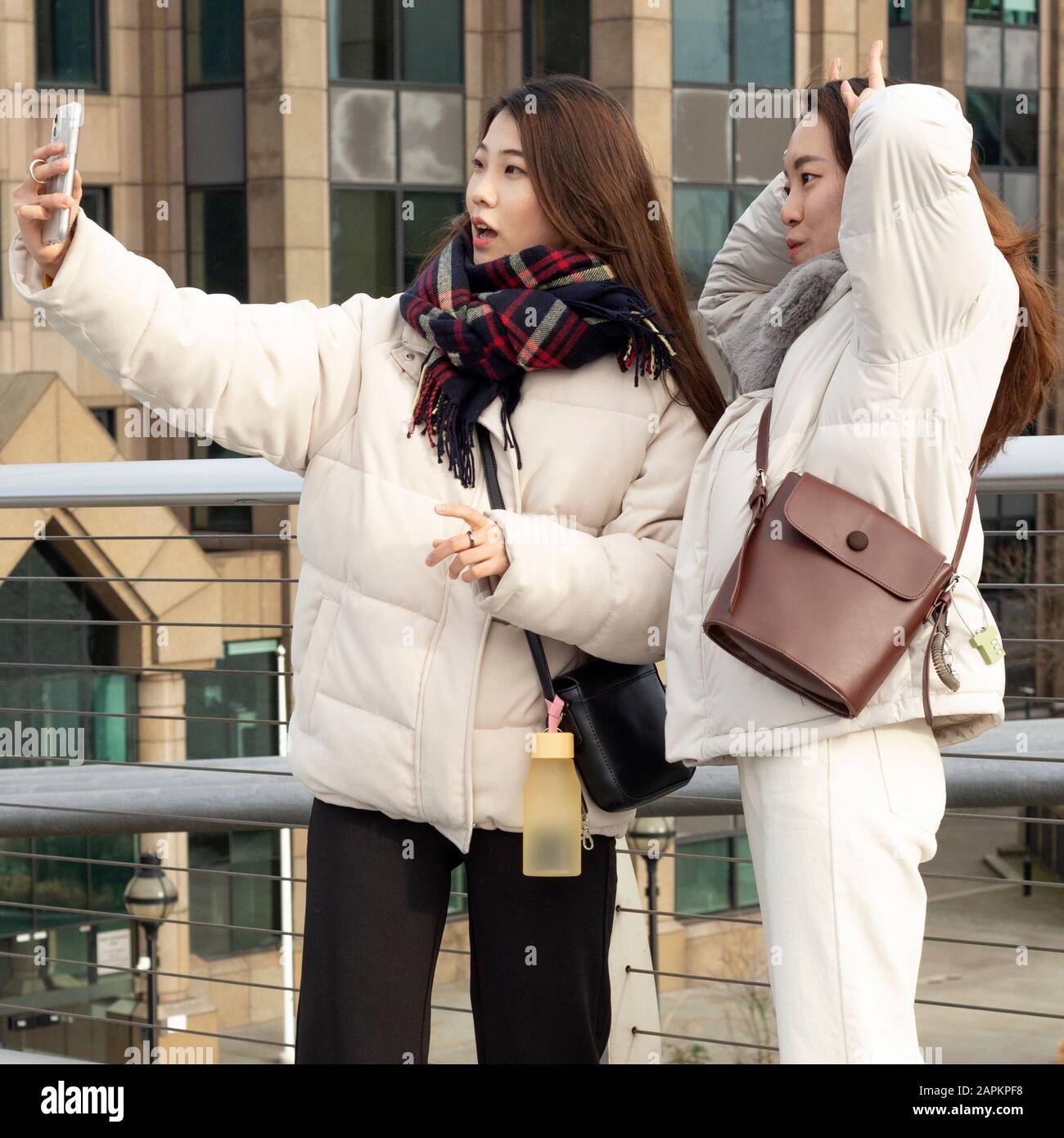 Due giovani donne asiatiche turisti sorridenti e in posa per scattare foto e scattare selfie sul Millennium Bridge di Londra, nel Regno Unito, a partire dal 2020 Foto Stock