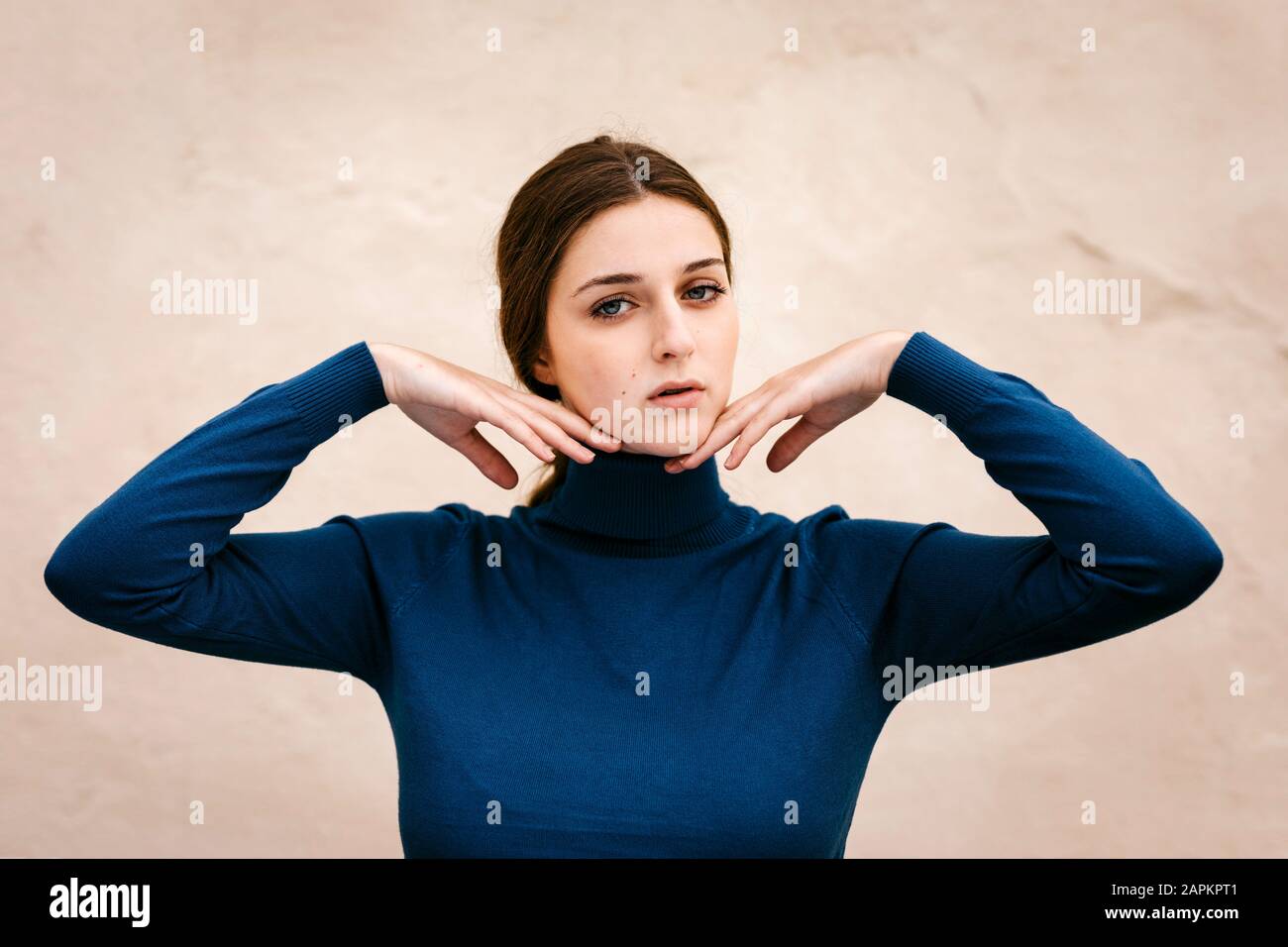 Primo piano ritratto di donna con turtleneck blu pullover, mani sul mento Foto Stock