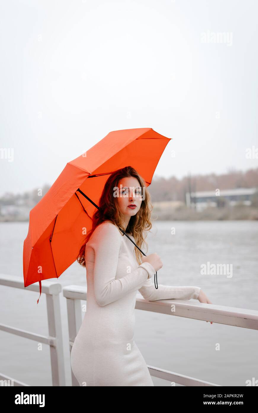 Ritratto di giovane donna con ombrello rosso, appoggiato sulla ringhiera durante il giorno delle piogge Foto Stock