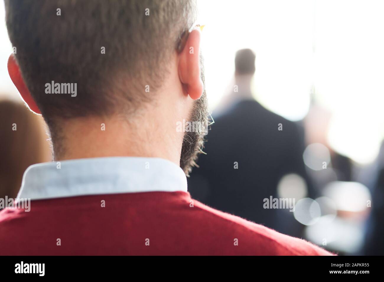 dietro la vista di un giovane uomo con la barba ad un raduno Foto Stock