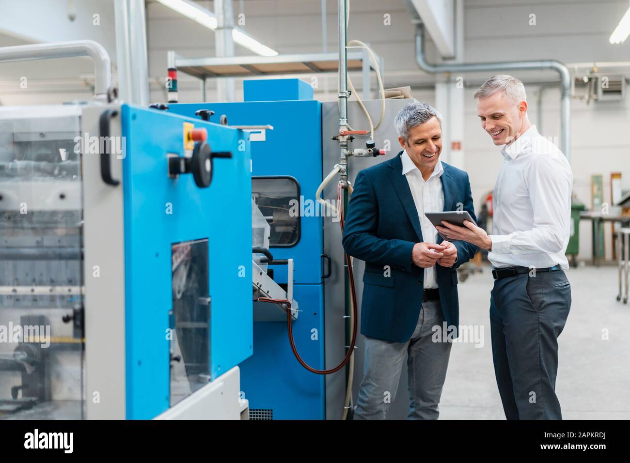 Due uomini d'affari sorridenti con tablet che parlano in una fabbrica Foto Stock