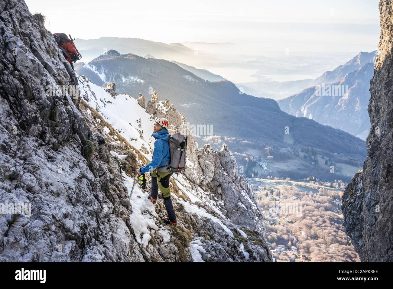 Alpinista in piedi in una montagna rocciosa innevata guardando in alto, Orobie Alpi, Lecco, Italia Foto Stock