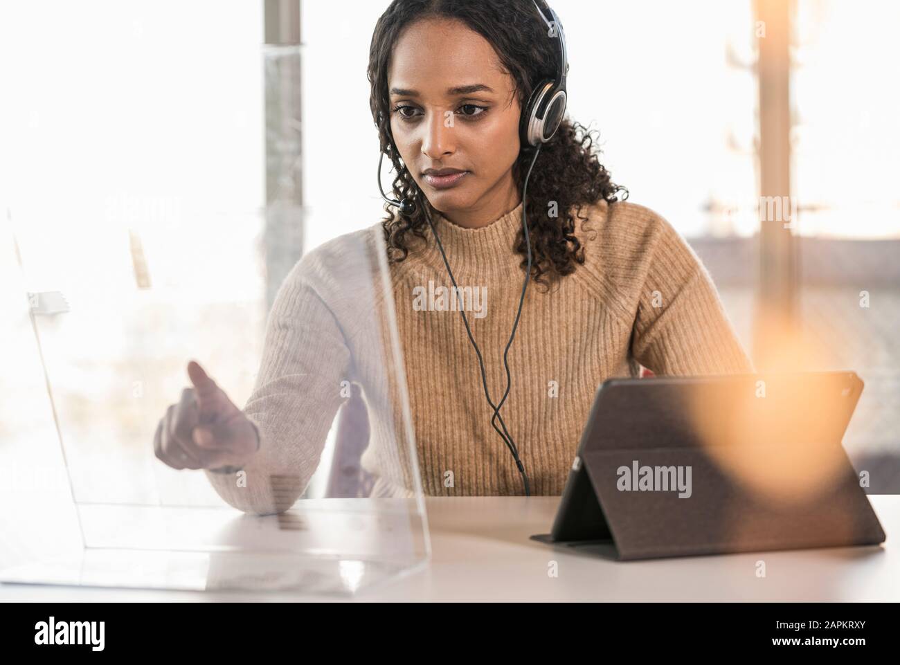 Giovane donna d'affari seduto alla scrivania in ufficio utilizzando uno schermo trasparente Foto Stock