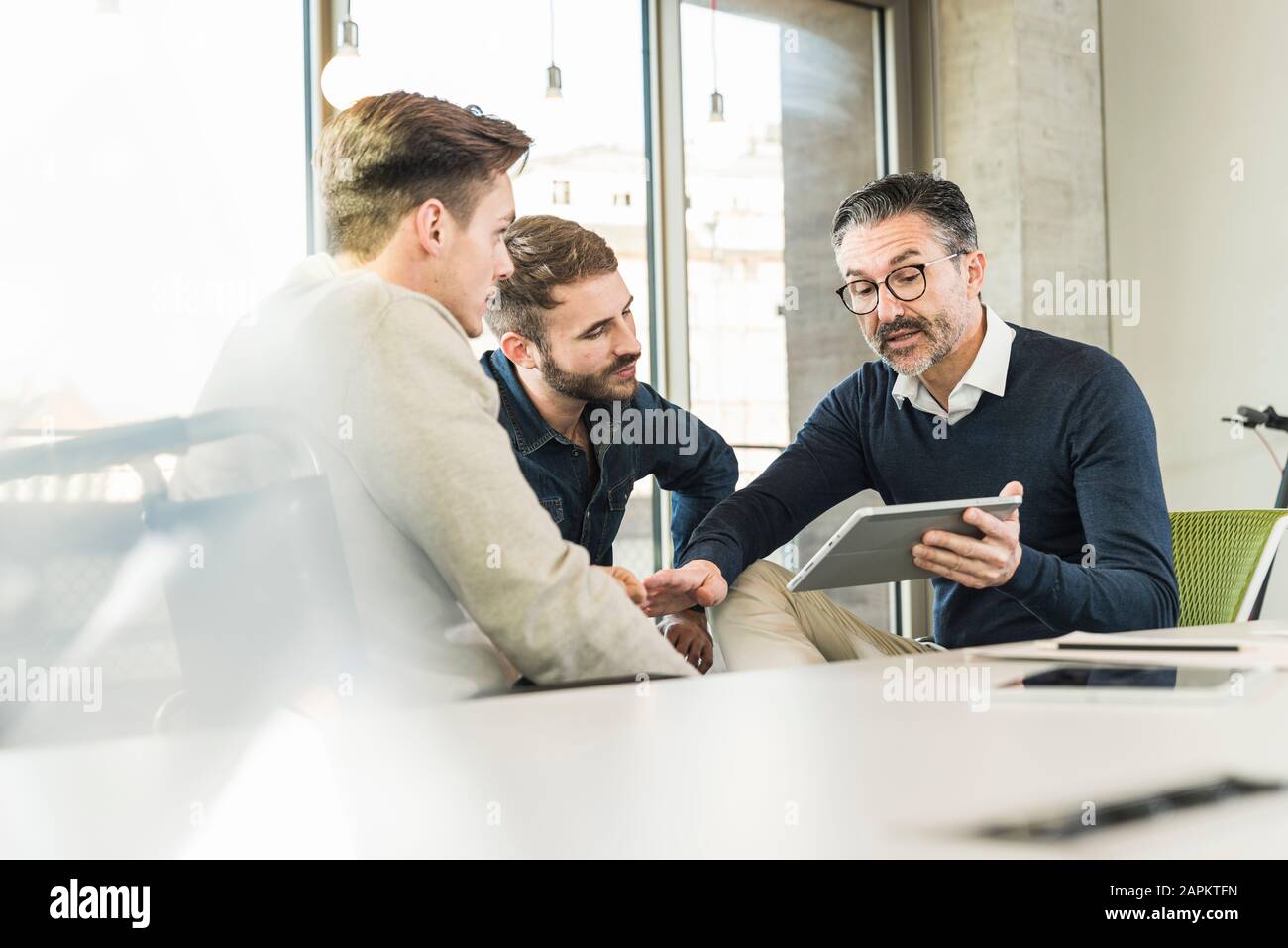 Tre uomini d'affari che hanno una riunione in ufficio che condividono un tablet Foto Stock