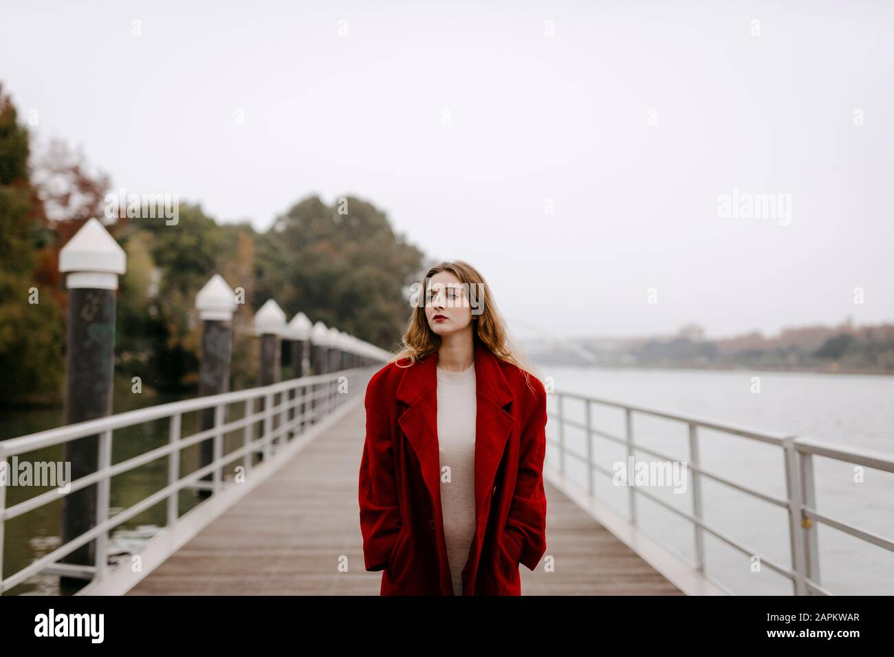 Ritratto di giovane donna che indossa cappotto rosso su un ponte durante il giorno di pioggia Foto Stock
