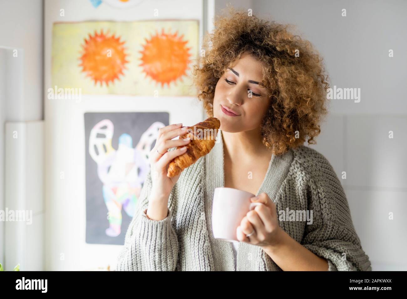 Donna che mangia croissant e beve caffè a casa Foto Stock