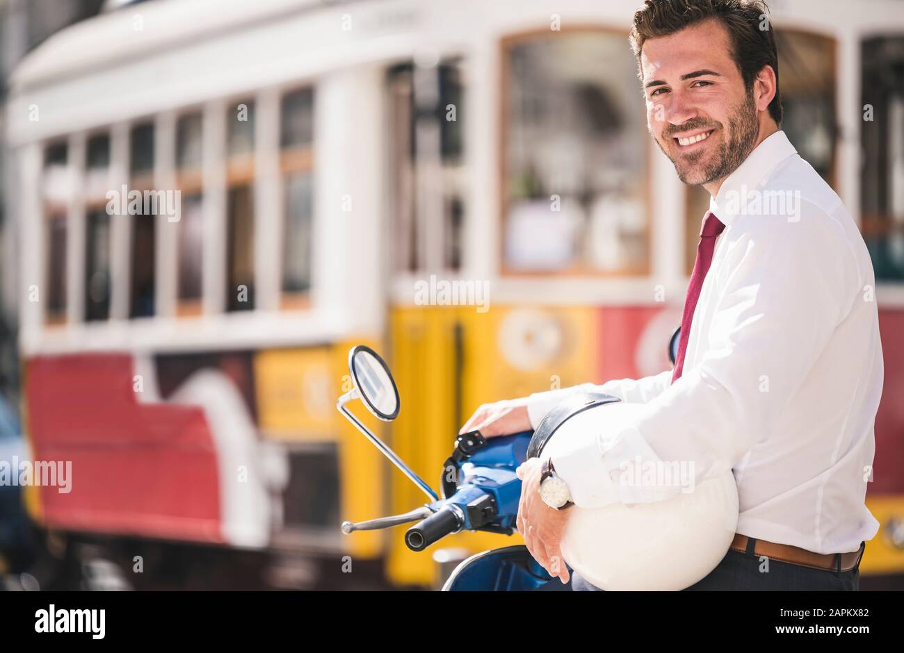 Ritratto di giovane uomo d'affari sorridente su scooter in città, Lisbona, Portogallo Foto Stock