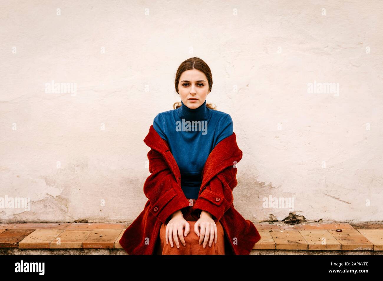 Primo piano ritratto di donna con turtleneck blu pullover e cappotto rosso seduto su un gradino Foto Stock