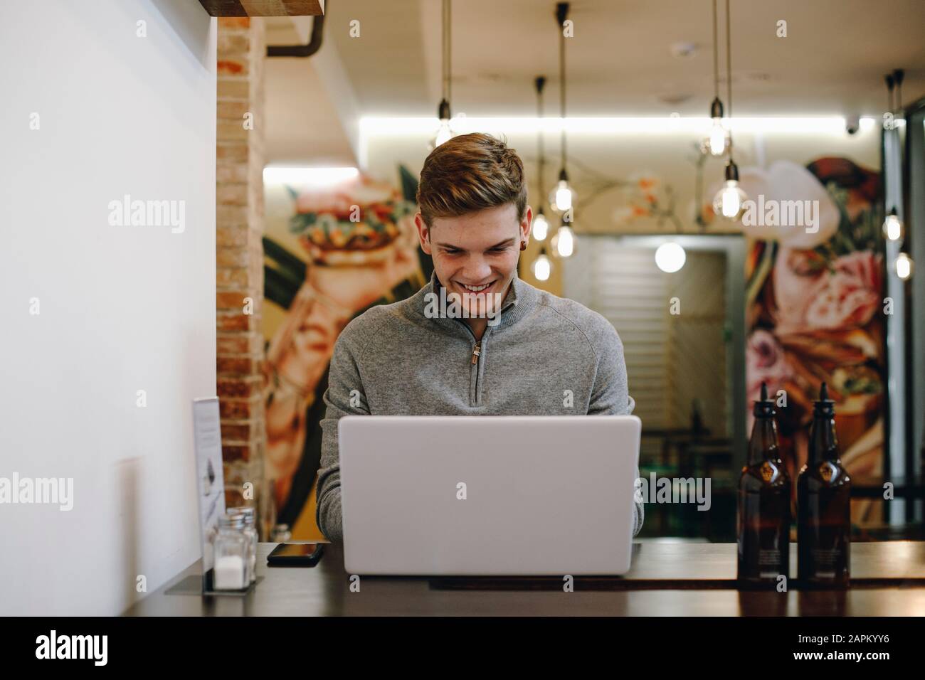 Giovane uomo seduto in un ristorante digitando sul suo portatile mentre sorridendo Foto Stock