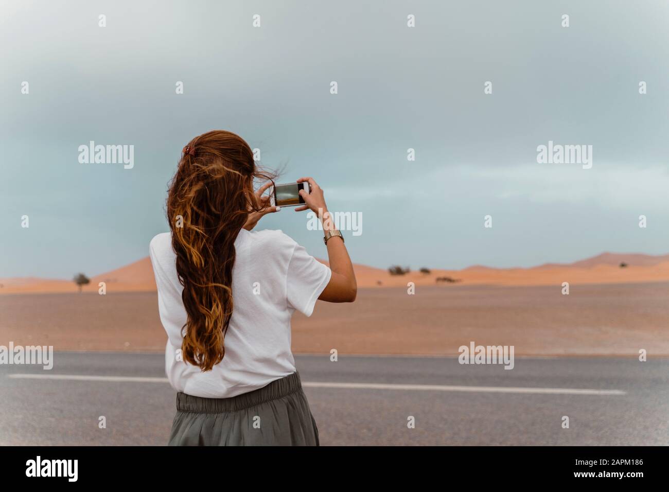Vista posteriore della giovane donna in piedi strada facendo foto con smartphone, Fez, Marocco Foto Stock