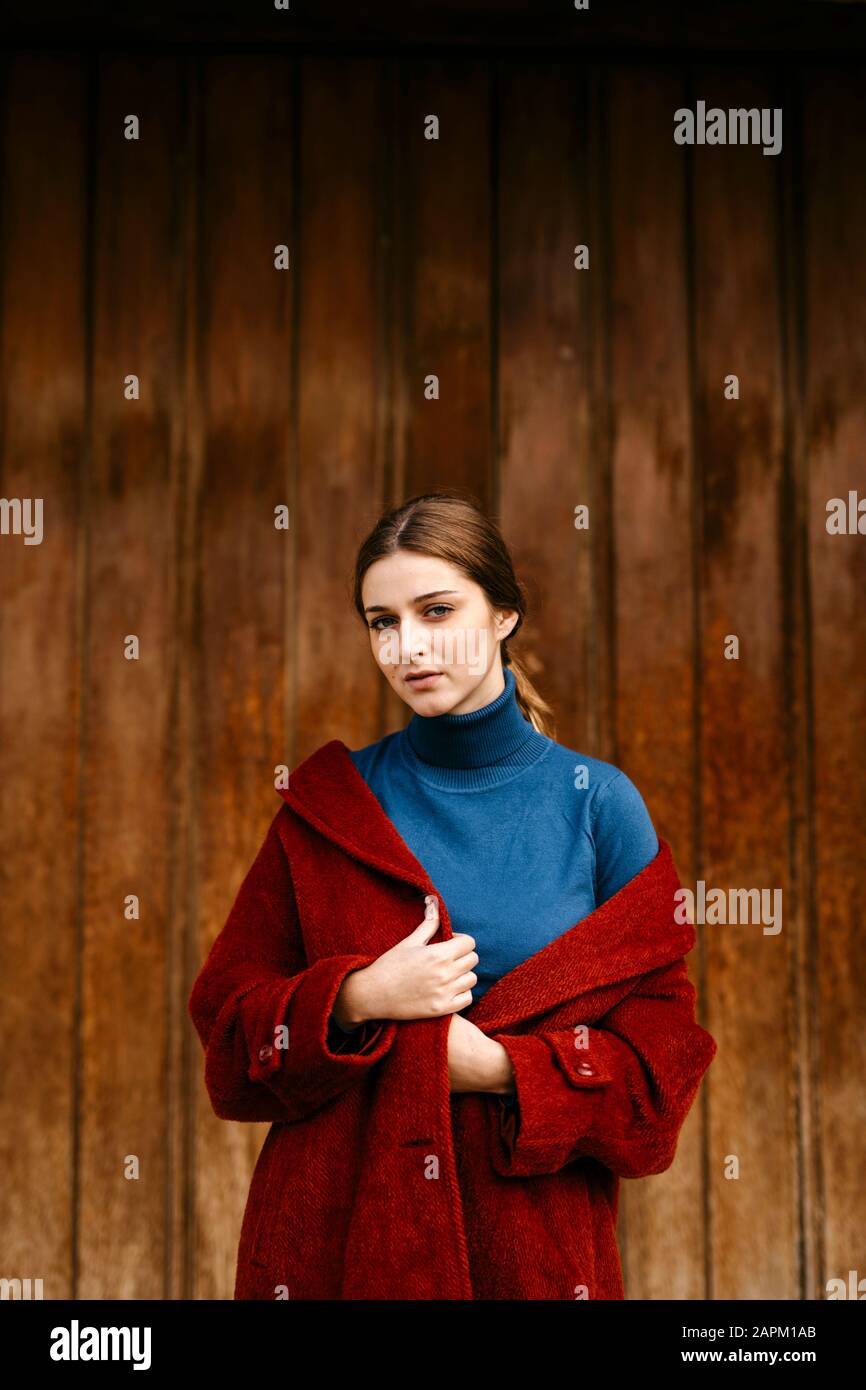 Primo piano ritratto di donna con turtleneck blu pullover e cappotto rosso di fronte a una porta di legno Foto Stock