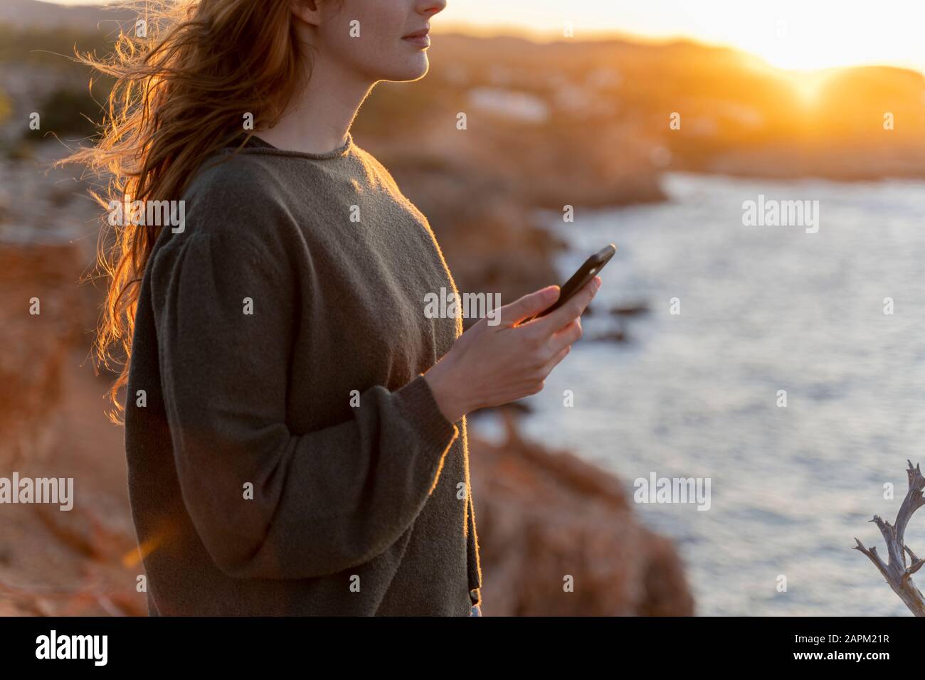 Giovane donna rossa con cellulare al tramonto, Ibiza, Spagna Foto Stock