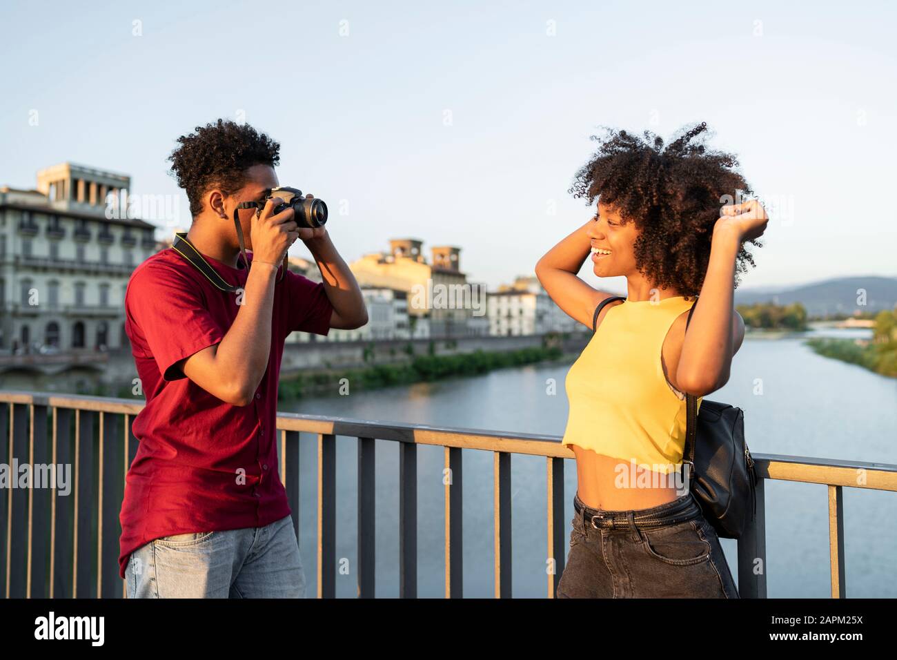 Giovane uomo che fa una foto della sua ragazza su un ponte sopra l'Arno al tramonto, Firenze, Italia Foto Stock