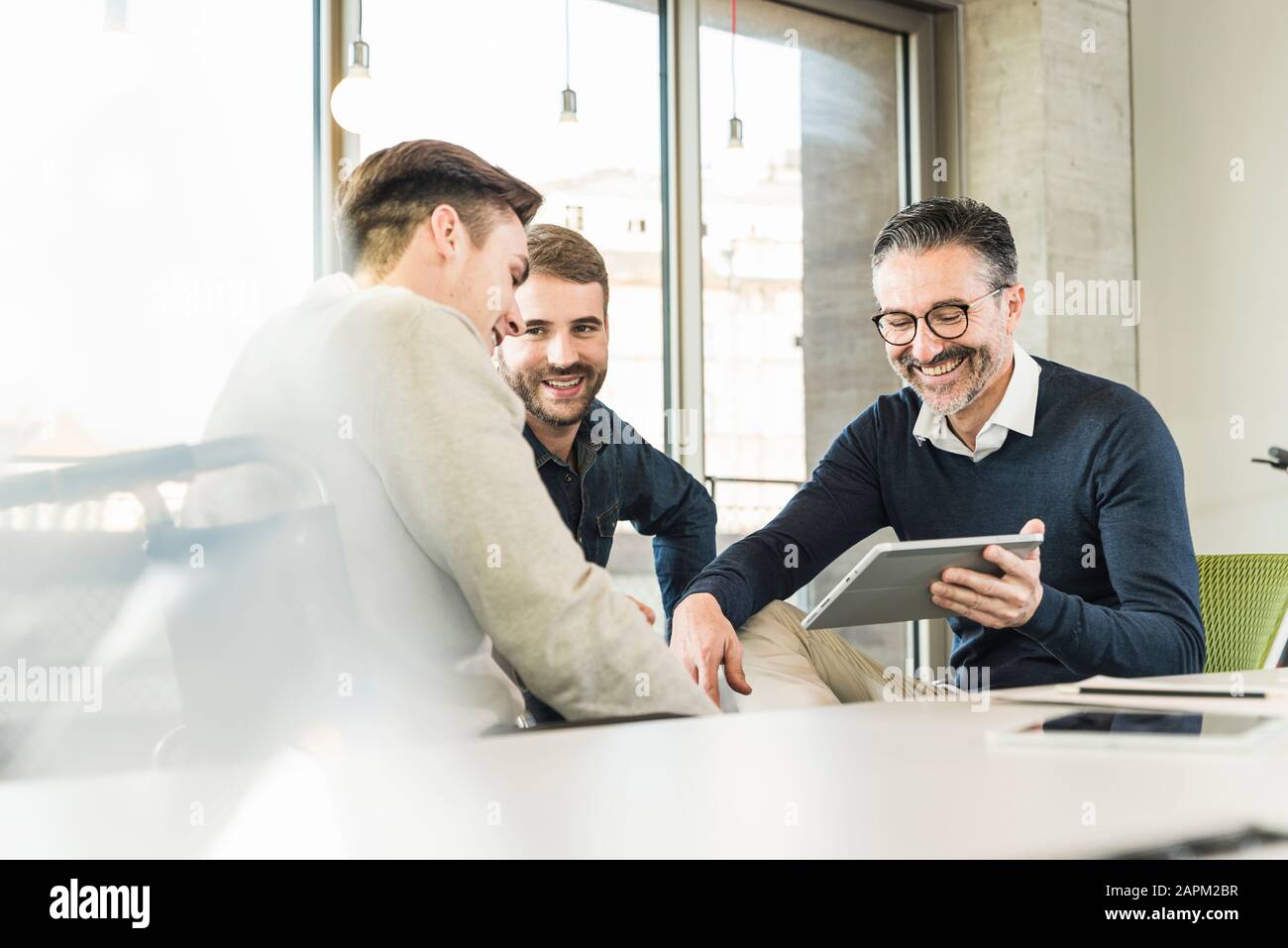 Tre uomini d'affari felici che hanno una riunione in ufficio che condivide un tablet Foto Stock