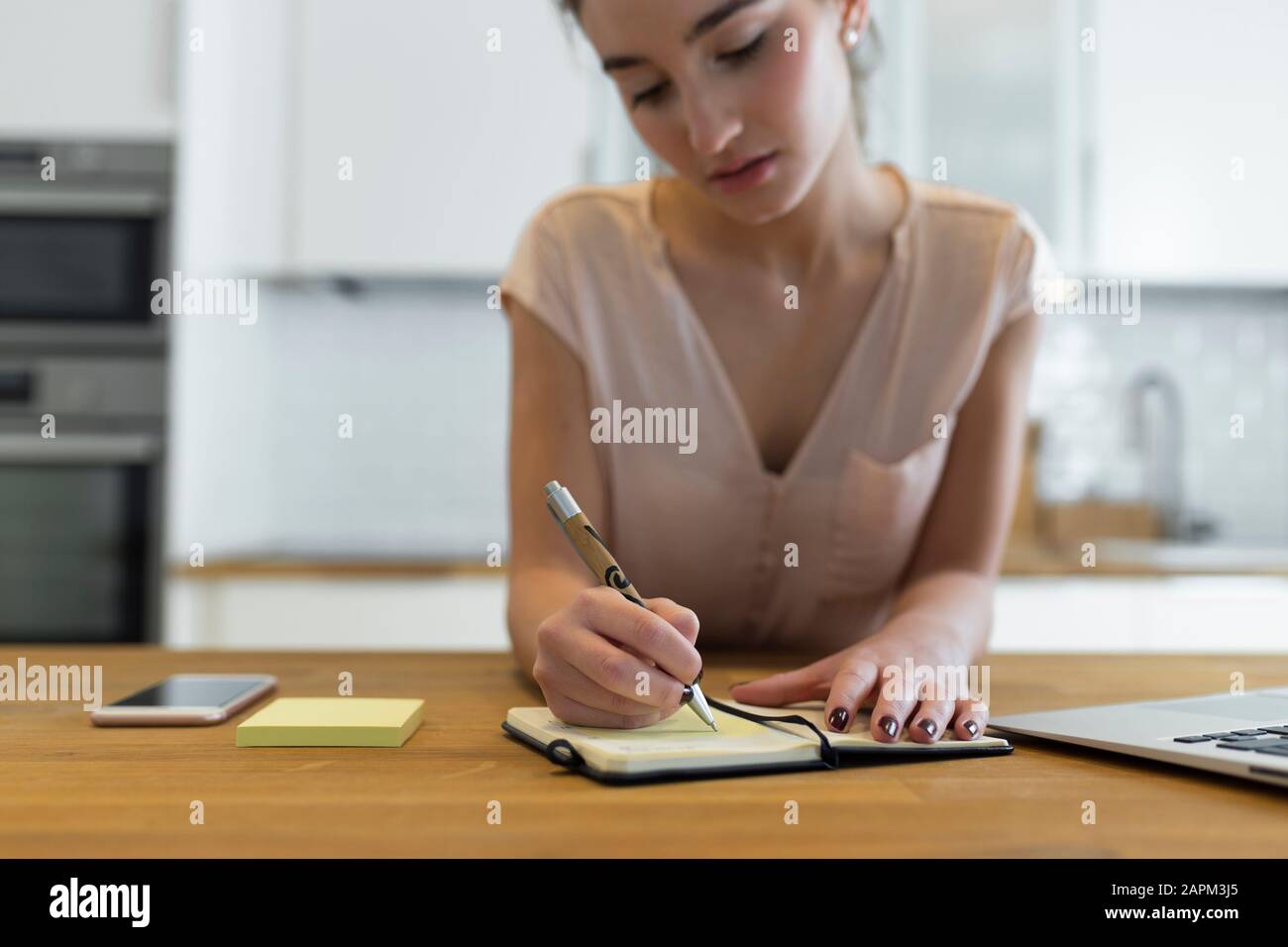 Adolescente femminile che scrive nel suo calendario in cucina Foto Stock