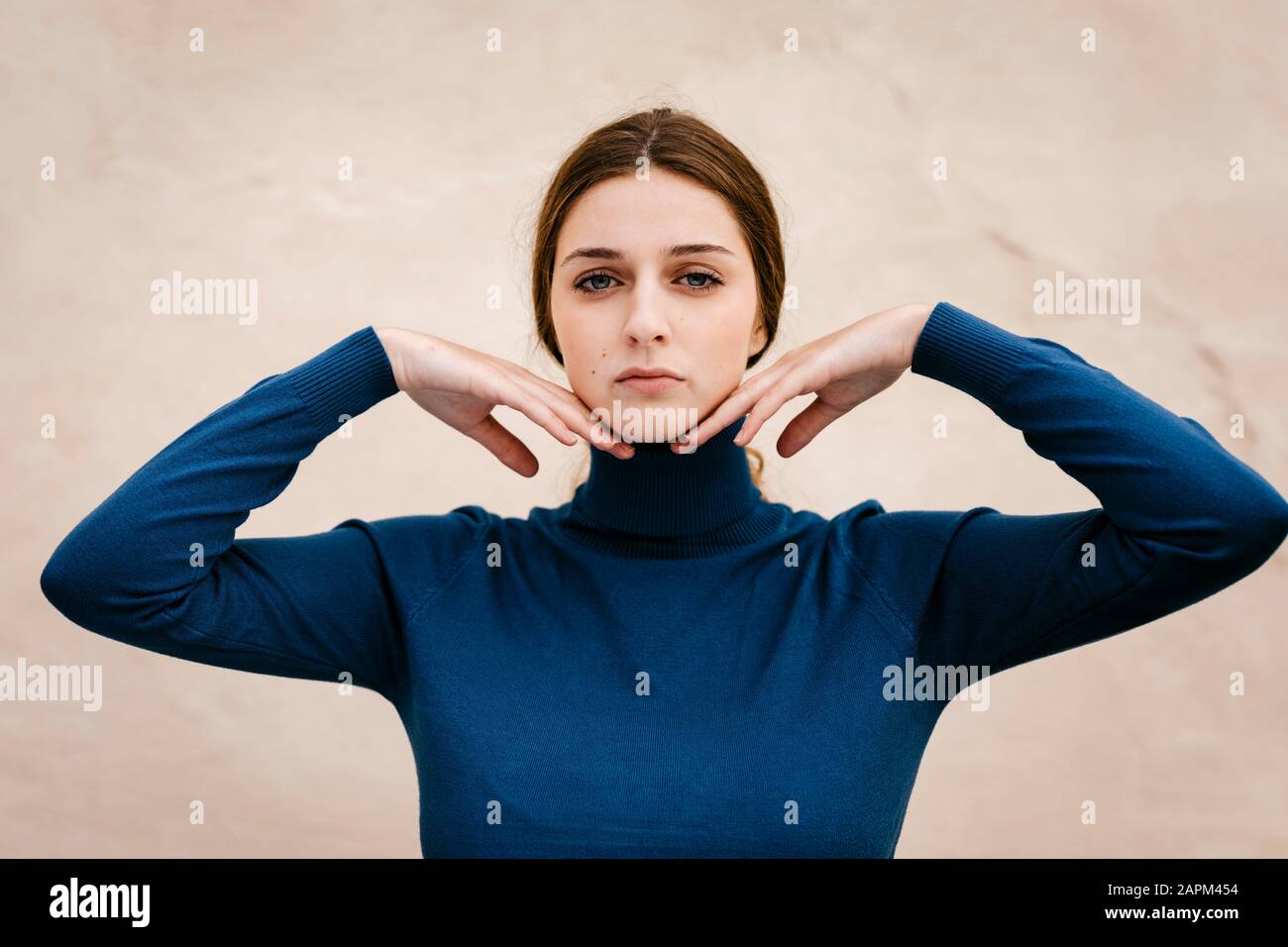 Primo piano ritratto di donna con turtleneck blu pullover, mani sul mento Foto Stock