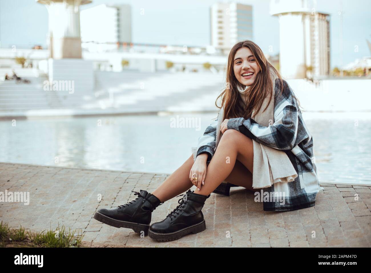 Giovane donna bruna con cappotto e sciarpa bianchi e neri in città Foto Stock