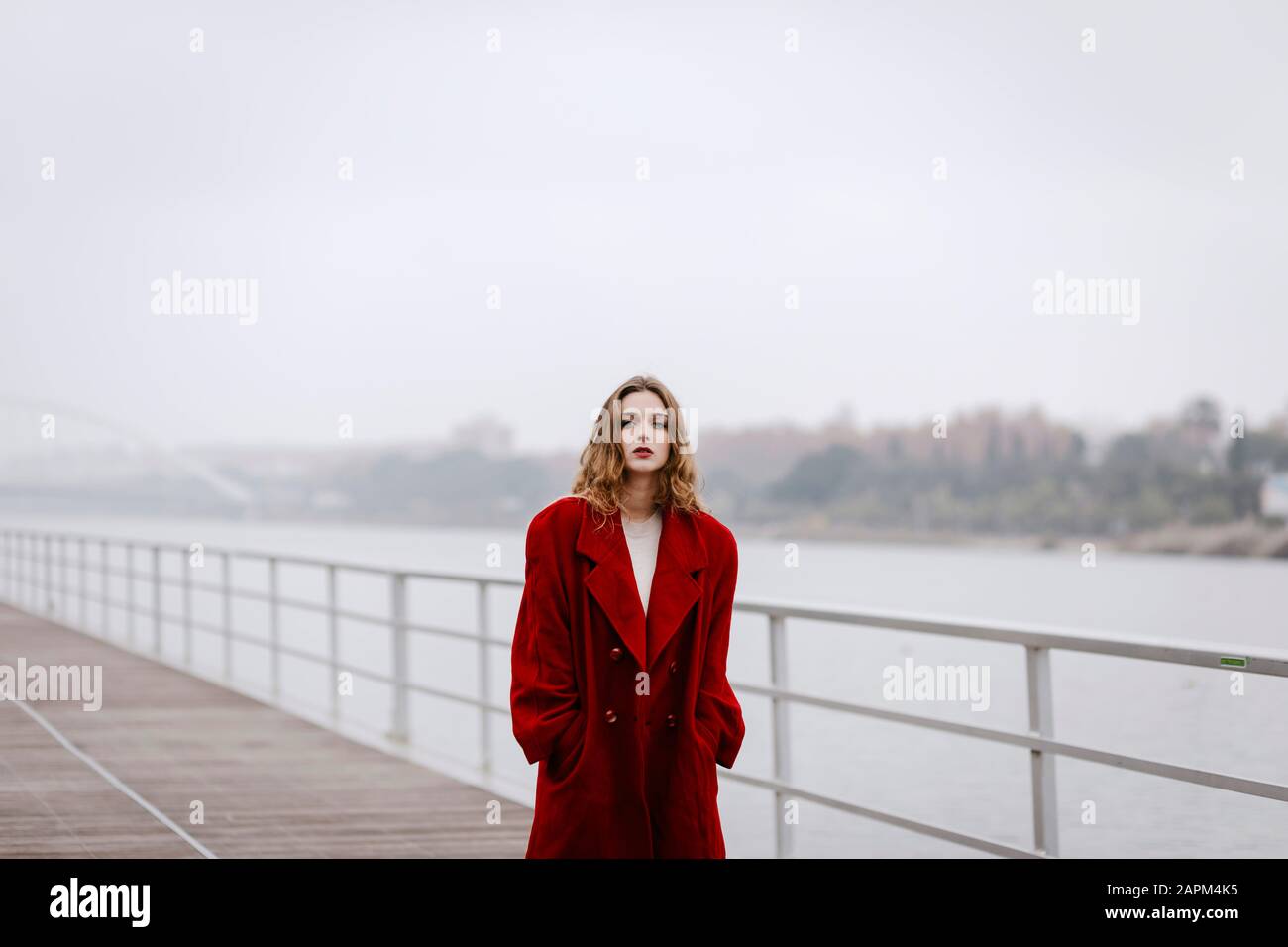 Ritratto di giovane donna che indossa cappotto rosso su un ponte durante il giorno di pioggia Foto Stock